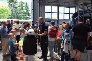 policjant pomaga założyć dziecku elementy umundurowania, obok stoją inne dzieci i dorośli