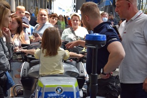 policjant stoi przy motocyklu, na którym siedzi dziewczynka, w tle ludzie