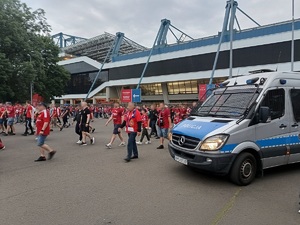 policyjny radiowóz stojący przed stadionem Wisły oraz kibice wychodzący ze stadionu