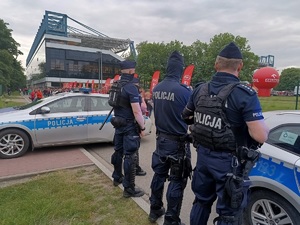 umundurowani policjanci stojący obok radiowozów obserwują przemieszczjących się kibiców przy stadionie Wisły Kraków