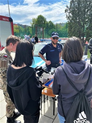 Policjant wraz grupką młodych ludzi przy stoisku profilaktycznym.