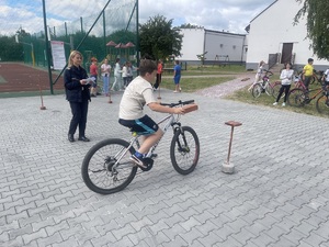 Policjantka sprawująca nadzór nad torem i chłopiec na rowerze, które próbuje umieścić cegiełkę na tyczce.