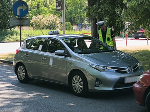 Policjant stojący przy taksówce od strony kierowcy prowadzi z kierowcą rozmowę