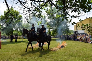 dwóch policjantów na koniach służbowych przemieszczających się obok palących elementów. Obok widać licznie zgromadzoną widownię