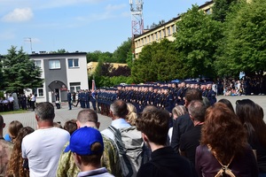 Na pierwszym planie widać gości odwiedzających katowicką szkołę stojących tyłem do zdjęcia. Przed nimi widać policjantów uczestniczących w uroczystej zbiórce