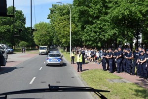 przez przednią szybę autobusu widać radiowóz oraz po prawej stronie policjantów i gości odwiedzających katowicą szkołę policji