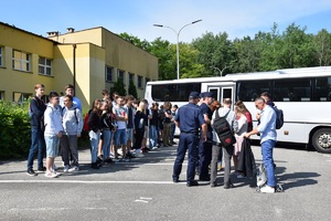 uczniowie w towarzystwie dwóch policjantów stoją na parkingu przed autobusem