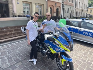 Mały chłopiec siedzący na policyjnym motocyklu w towarzystwie rodziców. Obok widać stojący policyjny radiowóz