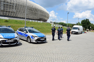 czterech umundurowanych policjantów patrolujących rejon Tauron Areny. Po lewej stronie widać dwa oznakowane radiowozy