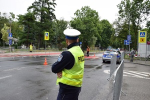 policjant ruchu drogowego stojący przy ulicy obserwuje okolice. W oddali widać policyjny radiowóz