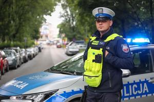 Umundurowany policjant ruchu drogowego stojący przed radiowozem.