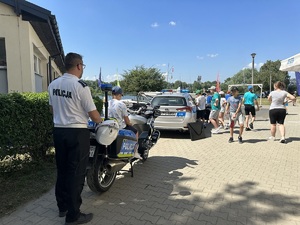 policjant ruchu drogowego obserwujący chłopca siedzącego na policyjnym motocyklu oraz grupę osób oglądającą radiowóz