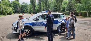 umundurowany policjant prezentuje grupie dzieci policyjny radiowóz