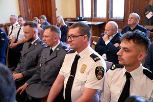 Na pierwszym planie widać siedzących dwóch funkcjonariuszy straży miejskiej oraz dwóch nagrodzonych policjantów. Obok widać inne osoby biorące udział w uroczystości