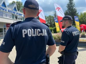 dwóch umundurowanych policjantów stojących tyłem do zdjęcia przed jednym z obiektów sportowych