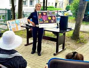 policjantka z plakatem  przypomina o  noszeniu elementów odblaskowych w tle budynek