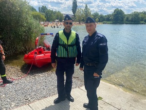 policjanci na brzegu zalewu w tle plażowicze