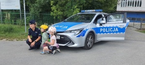 policjantka pozuje do zdjęcia z chłopcem i dziewczynką na tle radiowozu