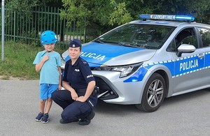 policjantka pozuje do zdjęcia z chłopcem na  tle radiowozu .