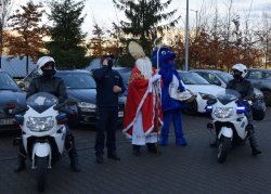 Mikołaj wraz z Inpektorem Wawelkiem, policjantem prewencji oraz dwoma policjantami drogówki, którzy siedzą na policyjnych motocyklach przed budynkiem szpitala imienia Jana Pawła II machają do dzieci w oknach