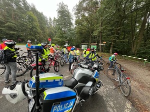 grupa uczestników przejazdu rowerowego na parkingu przy trasie przejazdu, na pierwszym planie policyjny motocykl