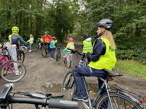 policjantka na rowerze wraz z grupą dzieci, rodziców i nauczycieli na skraju puszczy