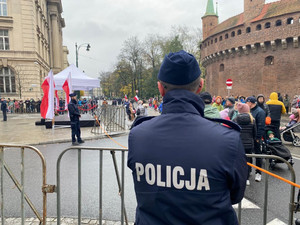 umundurowany policjnt stojący tyłem do zdjęcia obserwujący osoby znajdujące się na jednej z ulic Krakowa