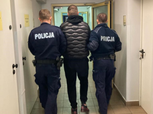 dwóch policjantów umundurowanych prowadzi zatrzymanego przez korytarz policyjnej jednostki