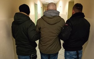 dwóch niemundurowanych policjantów prowadzi zatrzymanego mężczyznę przez korytarz policyjnej jednostki