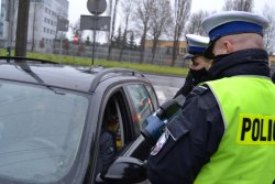 dwóch policjantów ruchu drogowego, jeden trzyma w ręku ręczny miernik prędkości tzw. radar stoją przy zatrzymanym do kontroli drogowej pojeździe.